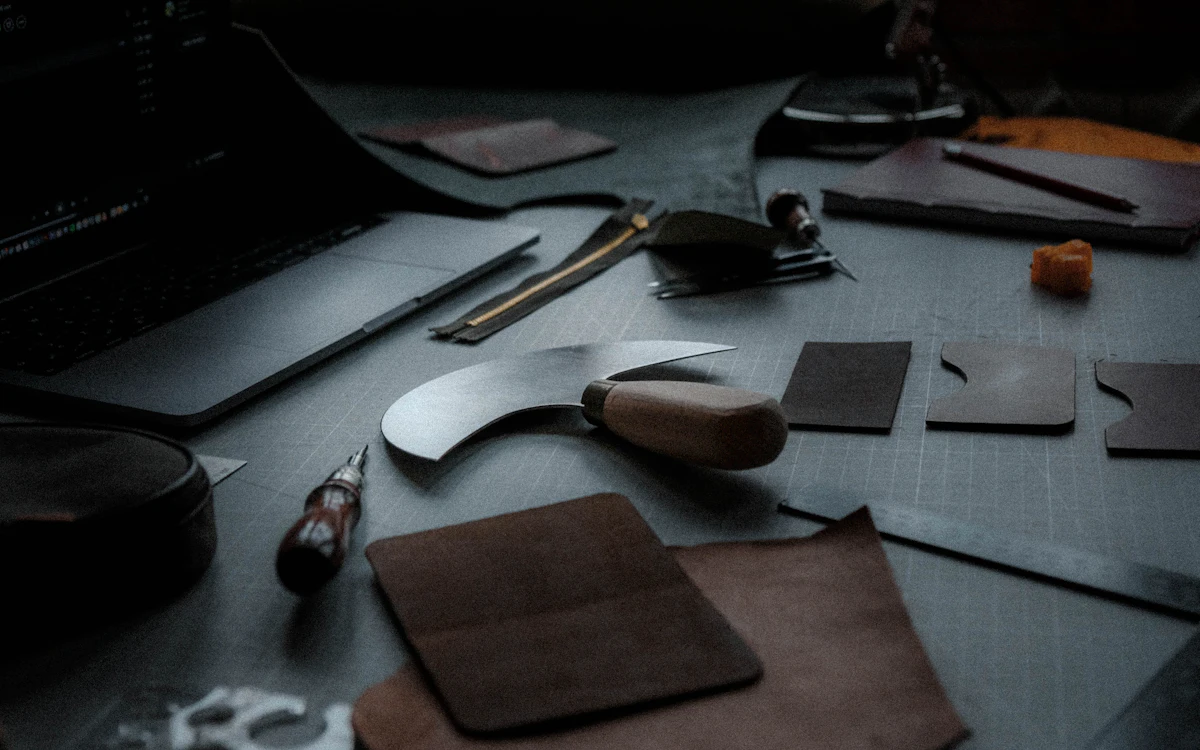 Dark artisan workbench with premium leather tools, swatches and a laptop — the craft behind Aryia Leather Co.